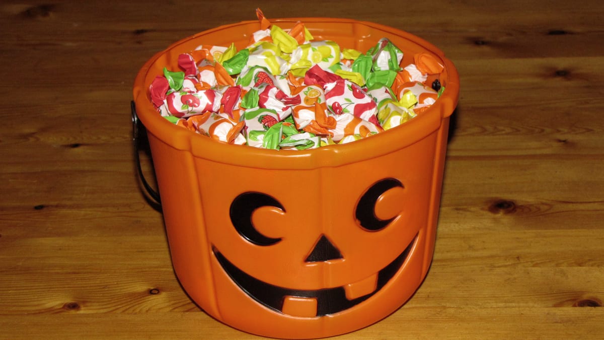 Cubeta naranja con forma de calabaza de Halloween llena de caramelos envueltos, sobre una mesa de madera