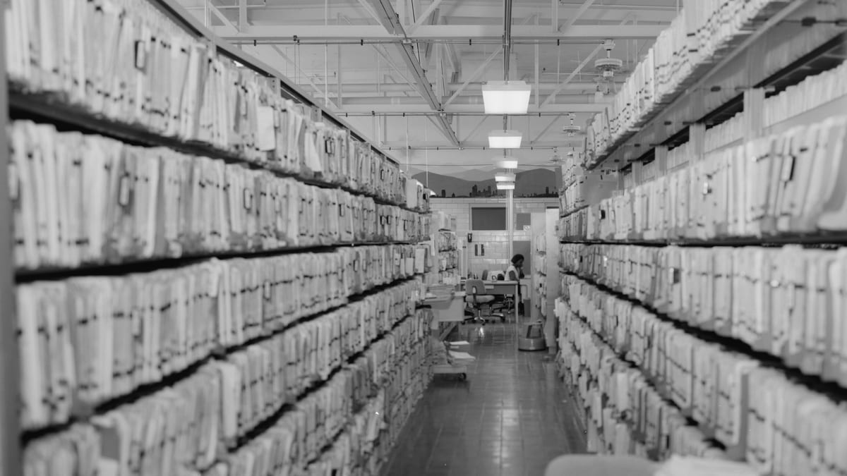 Pasillo de un archivo hospitalario con estantes llenos de expedientes clínicos en papel